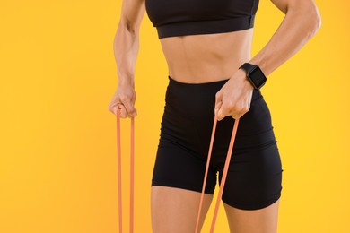 Woman exercising with elastic resistance band on orange background, closeup