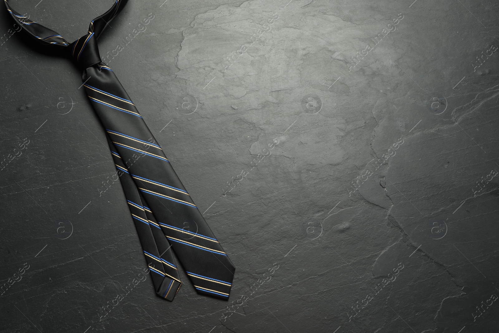 Photo of One striped necktie on grey textured table, top view. Space for text