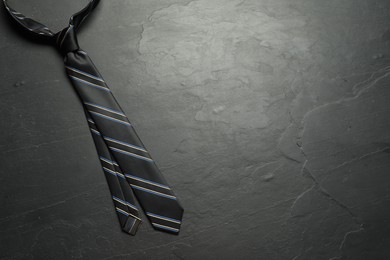 One striped necktie on grey textured table, top view. Space for text