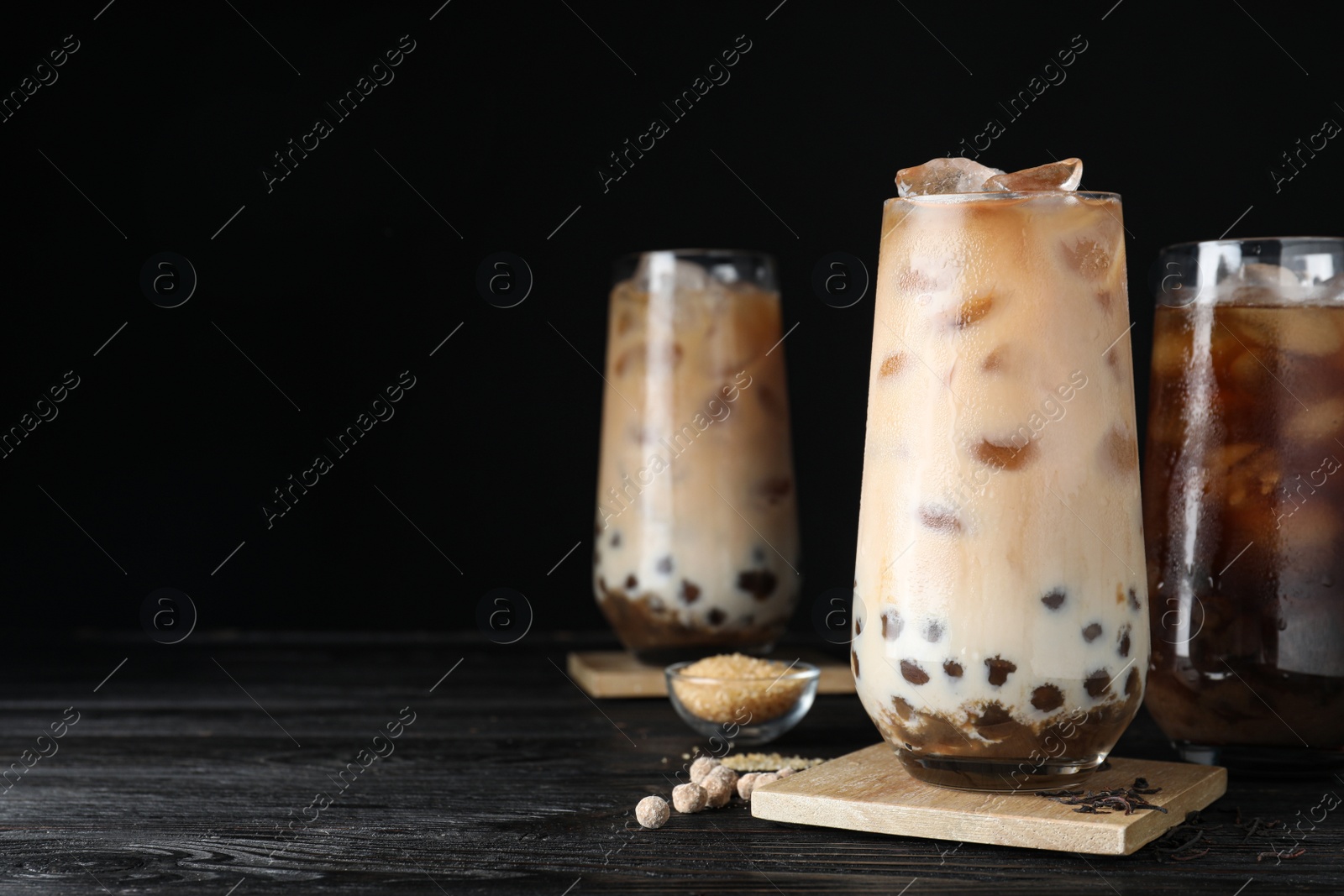 Photo of Tasty brown milk bubble tea on black wooden table. Space for text