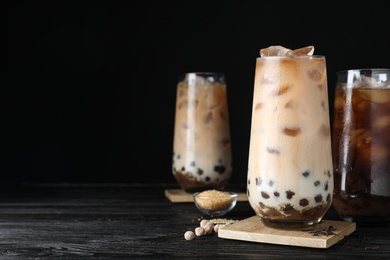 Photo of Tasty brown milk bubble tea on black wooden table. Space for text