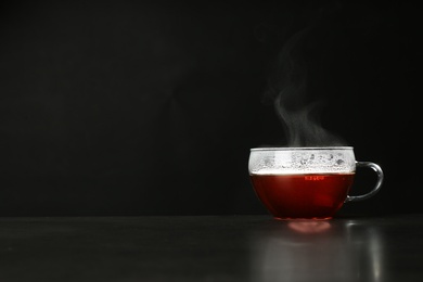 Photo of Glass cup with delicious hot tea on table against dark background. Space for text