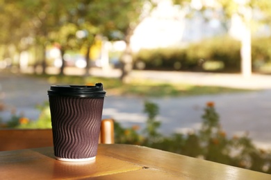 Cardboard coffee cup on wooden table outdoors. Space for text