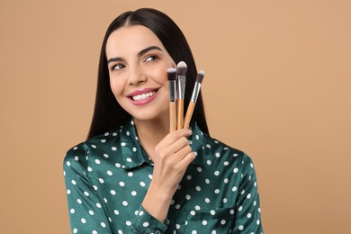 Happy woman with different makeup brushes on light brown background. Space for text
