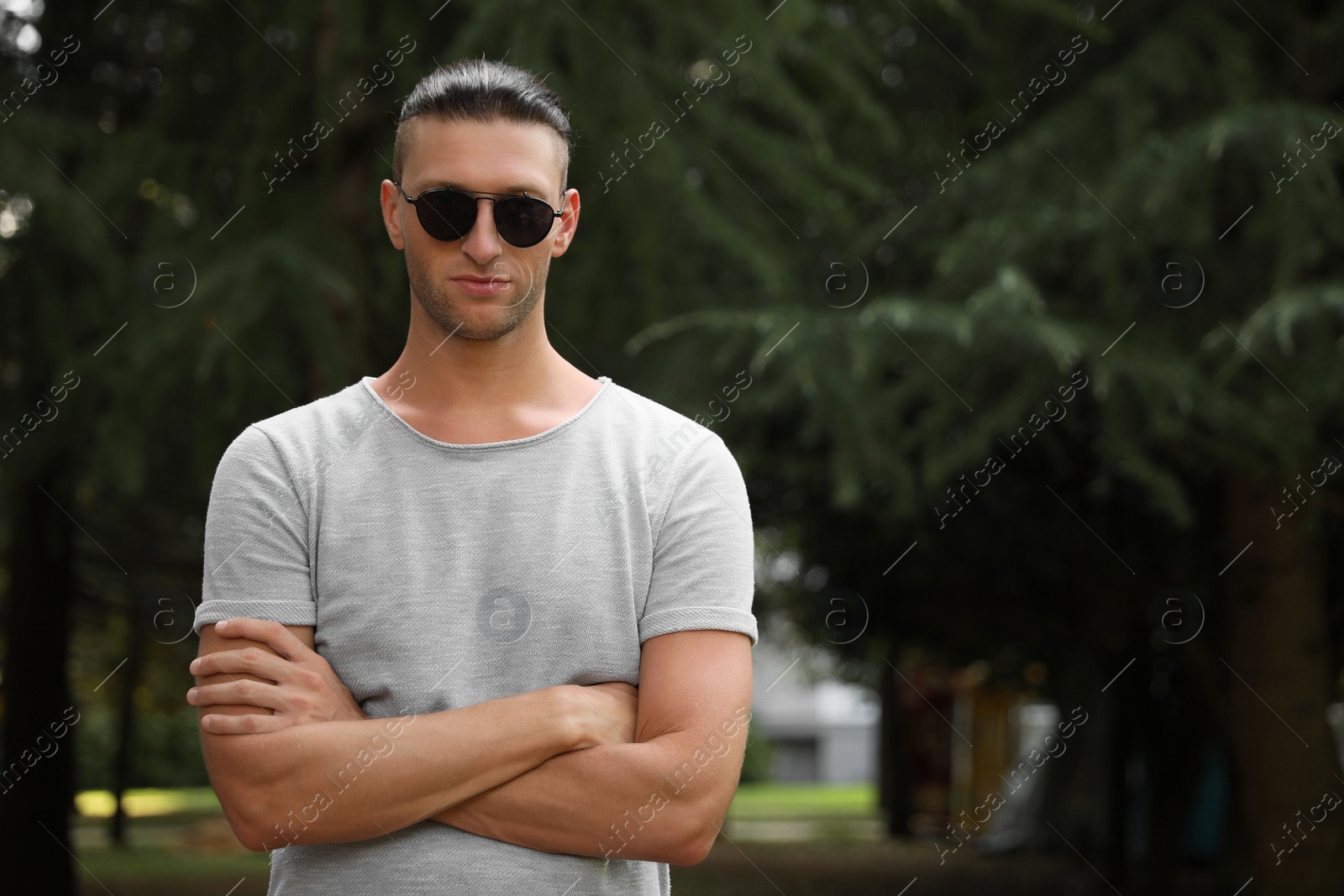 Photo of Handsome young man in stylish sunglasses at park, space for text