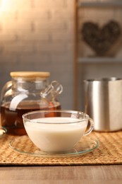 Photo of Tasty milk in glass cup, pitcher and teapot with tea on wooden table