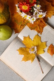 Book with autumn leaves and beautiful flowers as bookmark on light gray table, flat lay