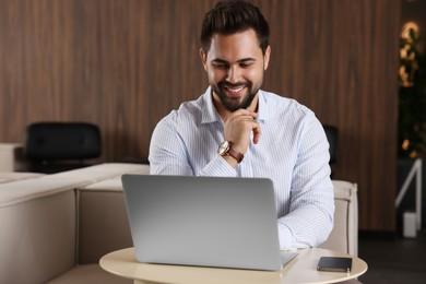 Happy young man working on laptop at table in office