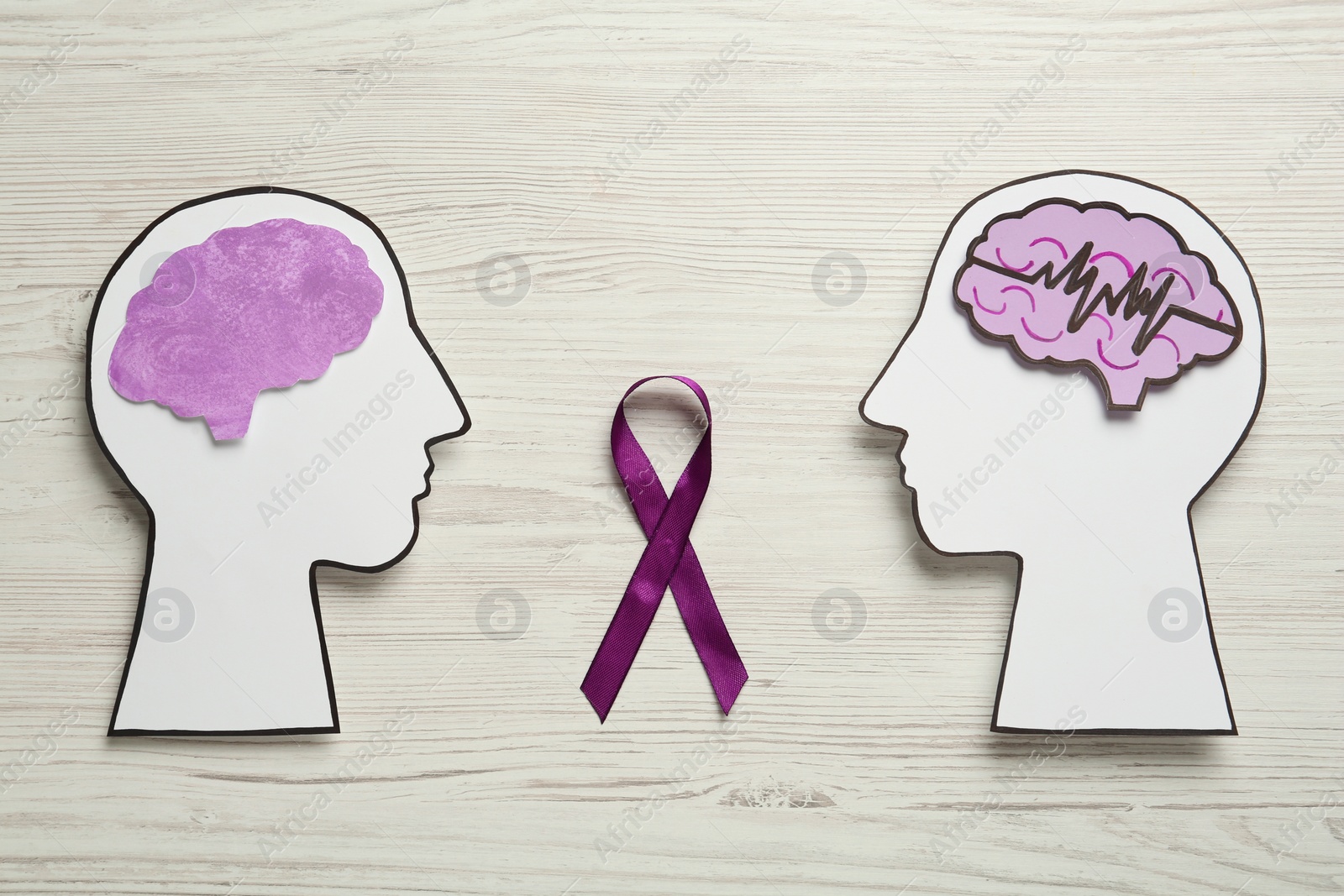 Photo of Human head cutouts with different brains and purple ribbon on white wooden background, flat lay. Epilepsy awareness