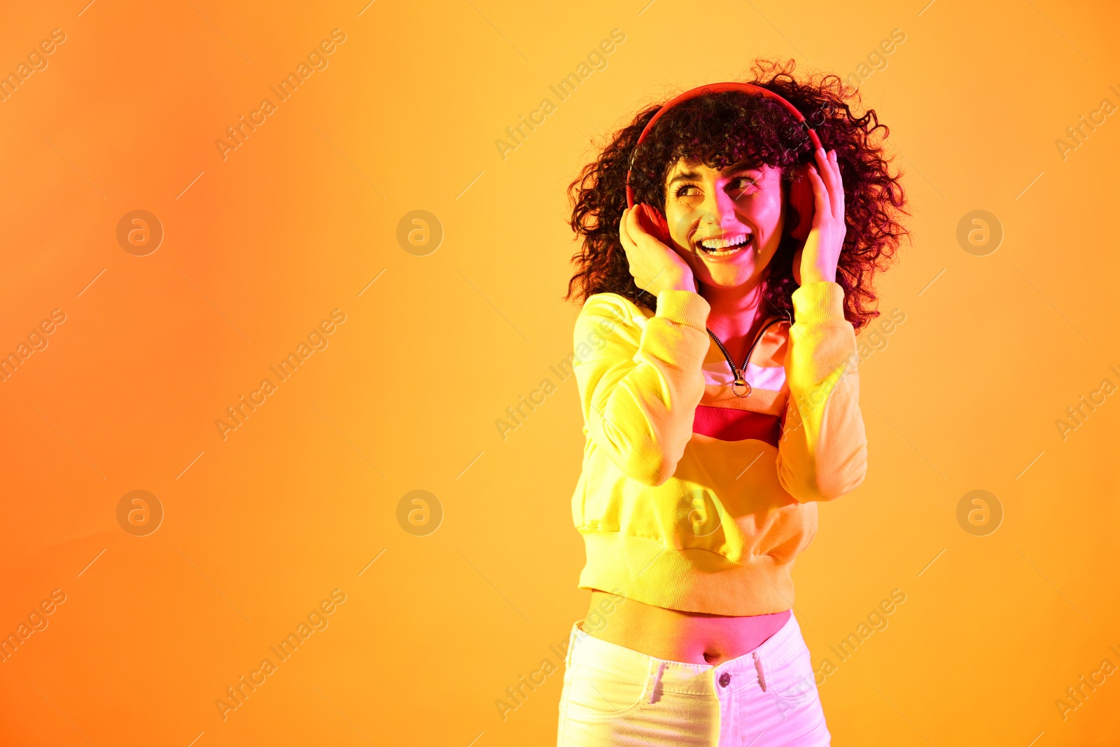 Photo of Beautiful young woman listening to music with headphones on color background in neon lights. Space for text