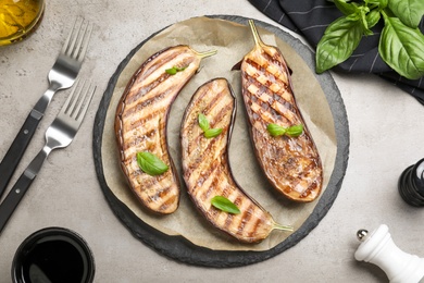 Photo of Delicious grilled eggplant halves with basil served on grey table, flat lay