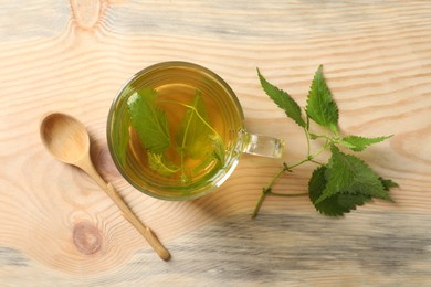 Photo of Glass cup of aromatic nettle tea and green leaves on wooden table, flat lay