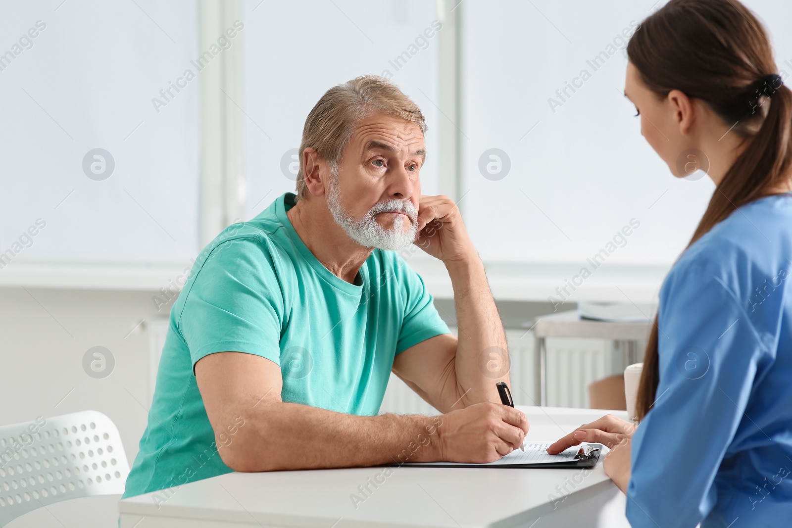 Photo of Doctor helping patient filling his medical card at table in clinic