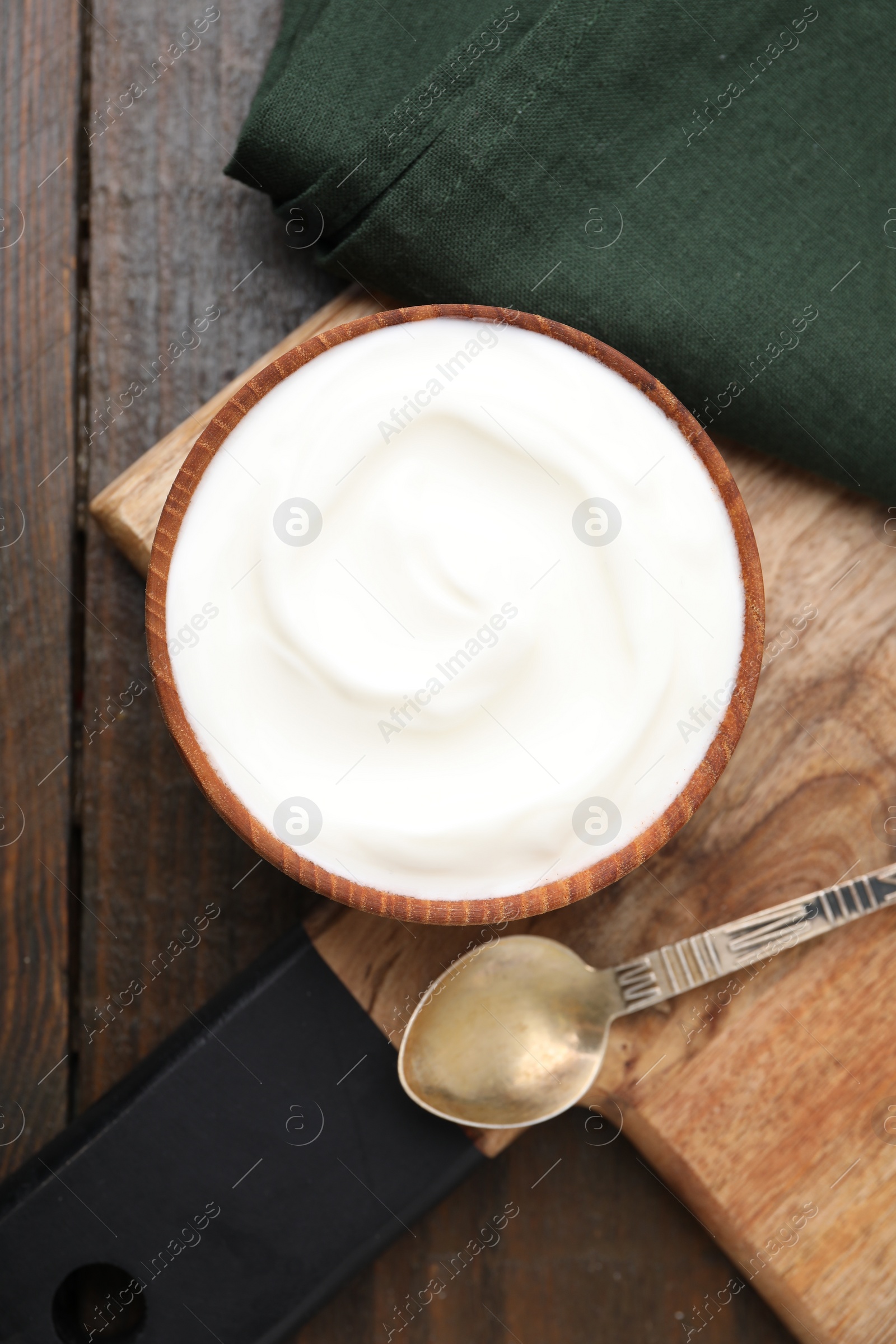 Photo of Delicious natural yogurt in bowl and spoon on wooden table, top view