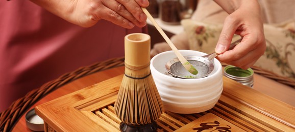 Woman preparing matcha drink at wooden table, closeup. Tea ceremony