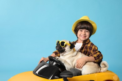 Photo of Little boy with his dog in toy car on light blue background