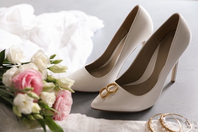 Composition with wedding dress, white high heel shoes and rings on grey background