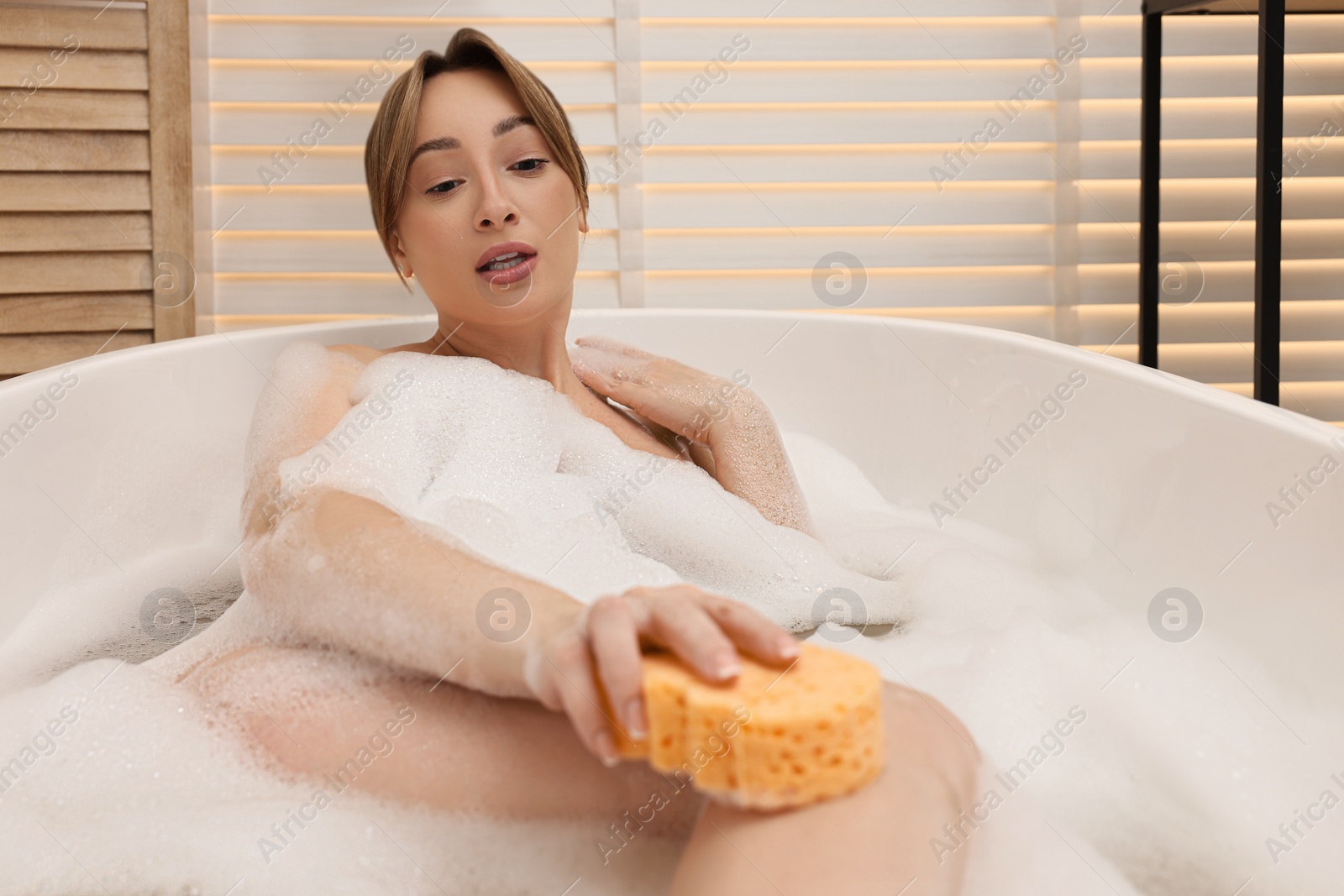 Photo of Beautiful woman taking bath with foam in tub indoors