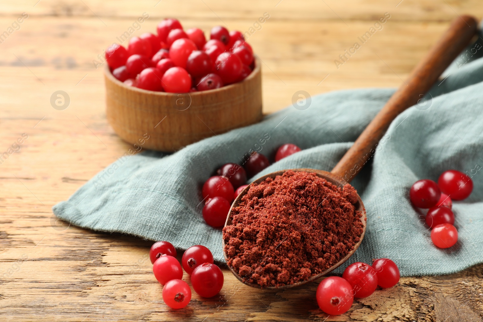 Photo of Spoon with cranberry powder and fresh berries on wooden table, closeup