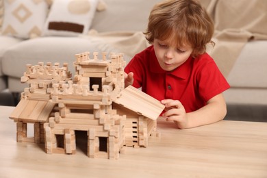 Cute little boy playing with wooden castle at table in room. Child's toy