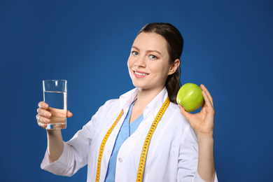 Photo of Nutritionist with glass of water and apple on blue background