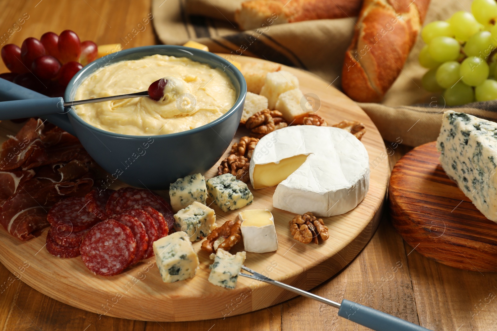 Photo of Fondue pot with tasty melted cheese, forks and different snacks on wooden table