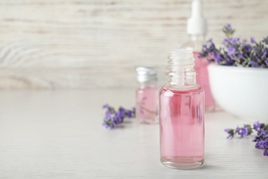 Bottles of essential oil and lavender flowers on white wooden table. Space for text