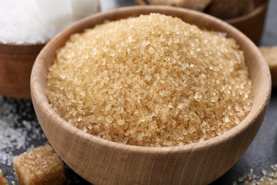 Photo of Brown granulated sugar in wooden bowl on black table, closeup