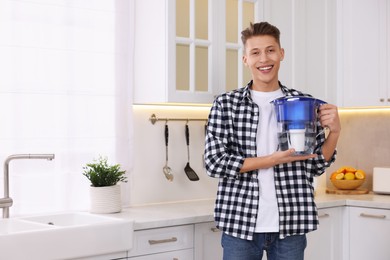 Happy man with water filter jug in kitchen. Space for text