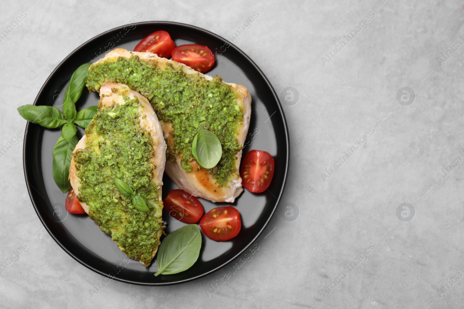 Photo of Delicious chicken breasts with pesto sauce, tomatoes and basil on light gray table, top view. Space for text
