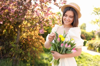 Photo of Beautiful young woman with bouquet of tulips in park on sunny day, space for text