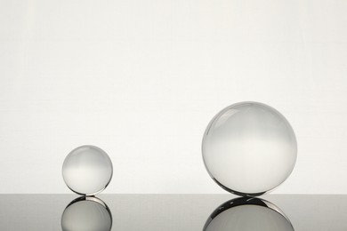 Photo of Transparent glass balls on mirror surface against light background. Space for text