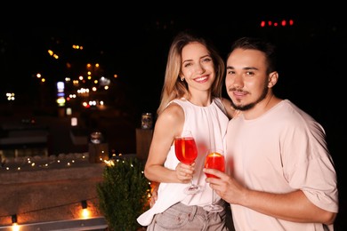 Photo of Romantic couple with glasses of cocktails on cafe terrace at night, space for text