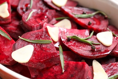 Raw beetroot slices, garlic and rosemary in baking dish, closeup