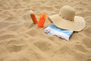 Photo of Sunscreens, hat and towel on sand, space for text. Sun protection care