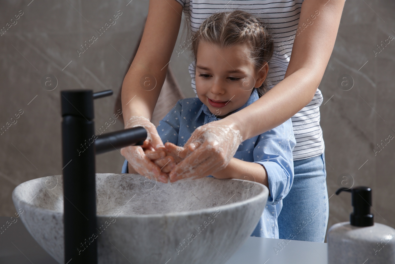 Photo of Mother and daughter washing hands with liquid soap together in bathroom, closeup