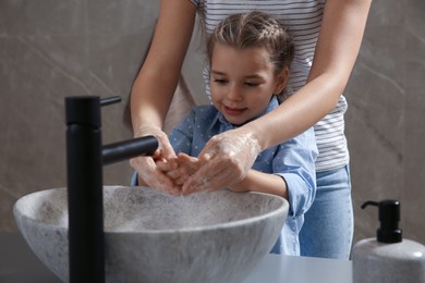 Photo of Mother and daughter washing hands with liquid soap together in bathroom, closeup