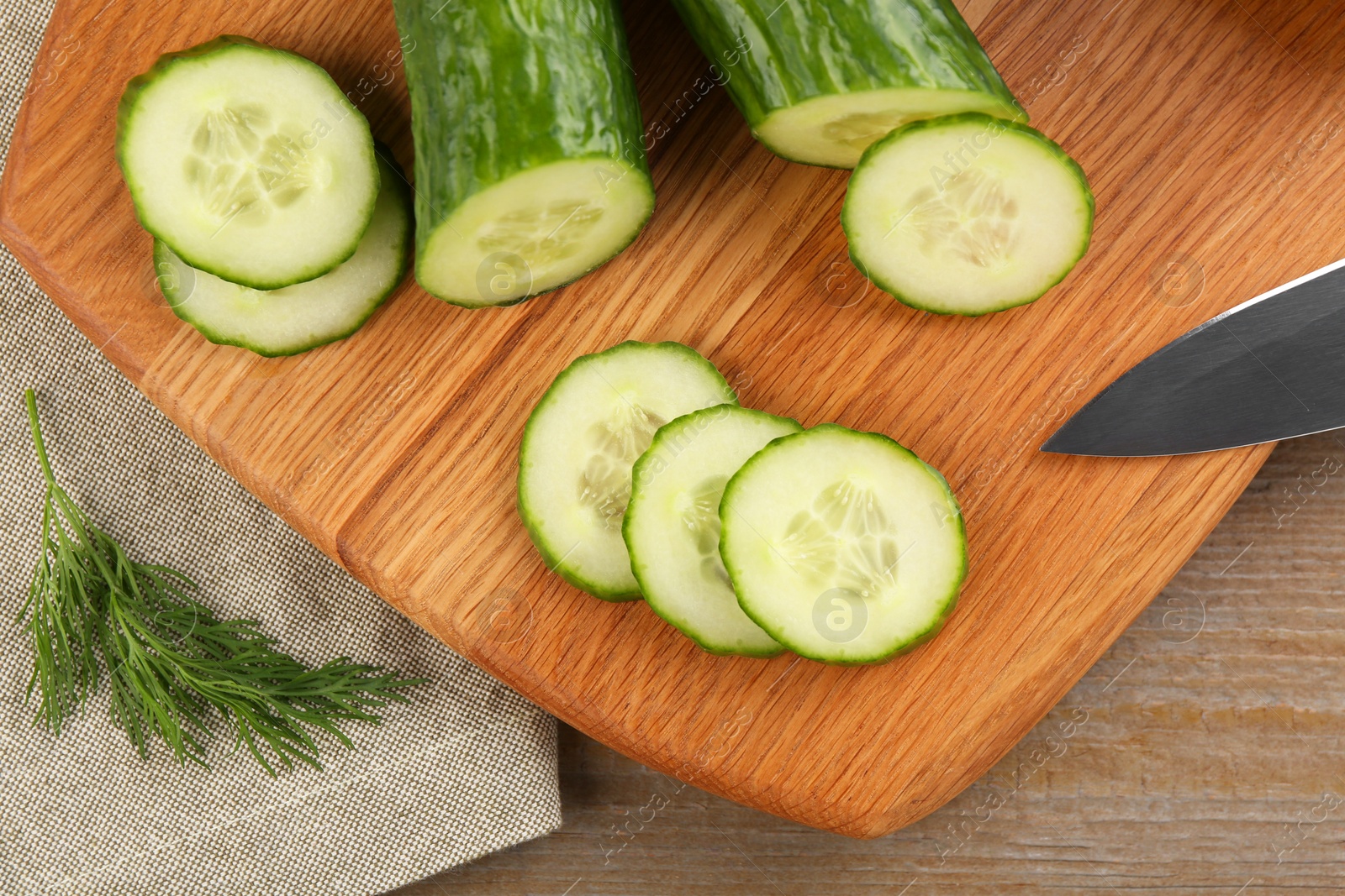Photo of Cucumbers, knife, cutting board and dill on wooden table, flat lay