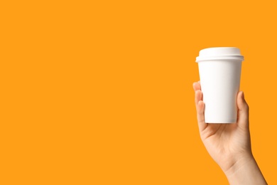 Woman holding takeaway paper coffee cup on orange background, closeup. Space for text