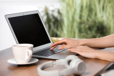 Photo of Woman working with laptop at wooden table, closeup