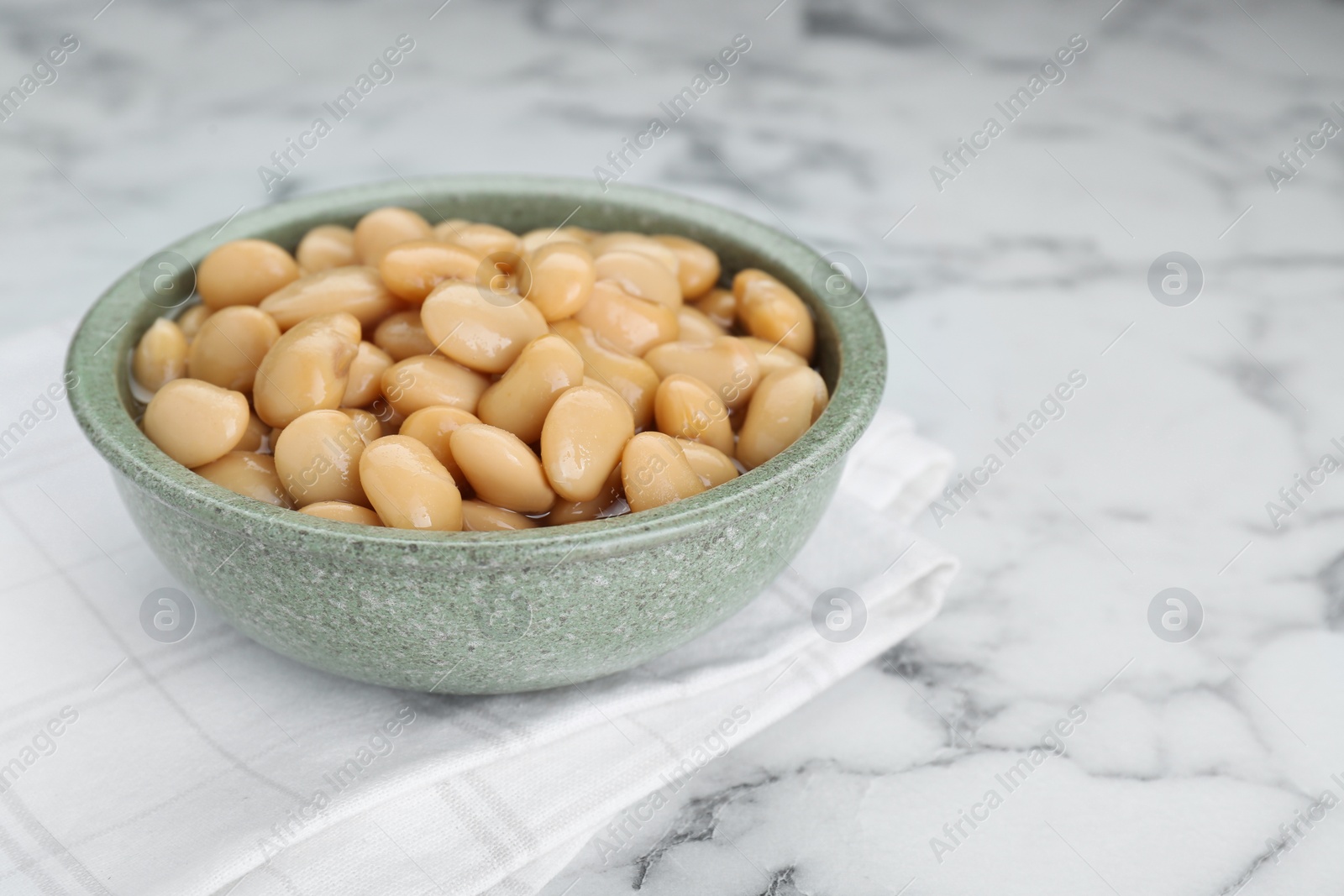 Photo of Bowl of canned kidney beans on white marble table, closeup. Space for text