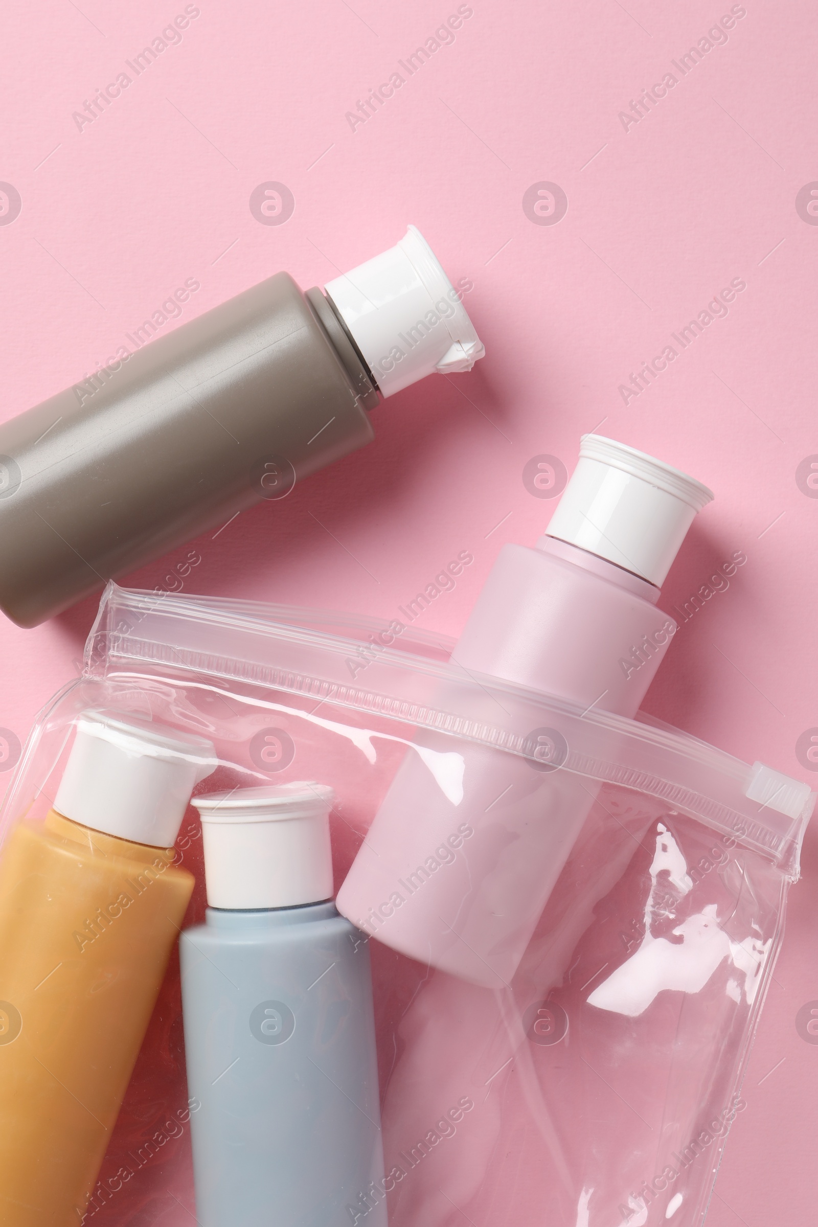 Photo of Plastic bag with cosmetic travel kit on pink background, flat lay. Bath accessories