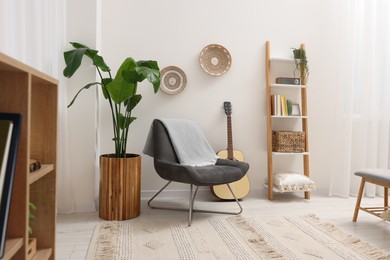 Spring atmosphere. Stylish room interior with comfortable chair, houseplant and shelving unit