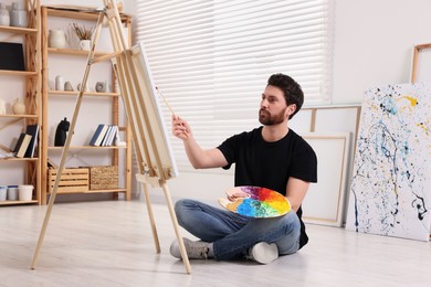 Photo of Man painting in studio. Using easel to hold canvas
