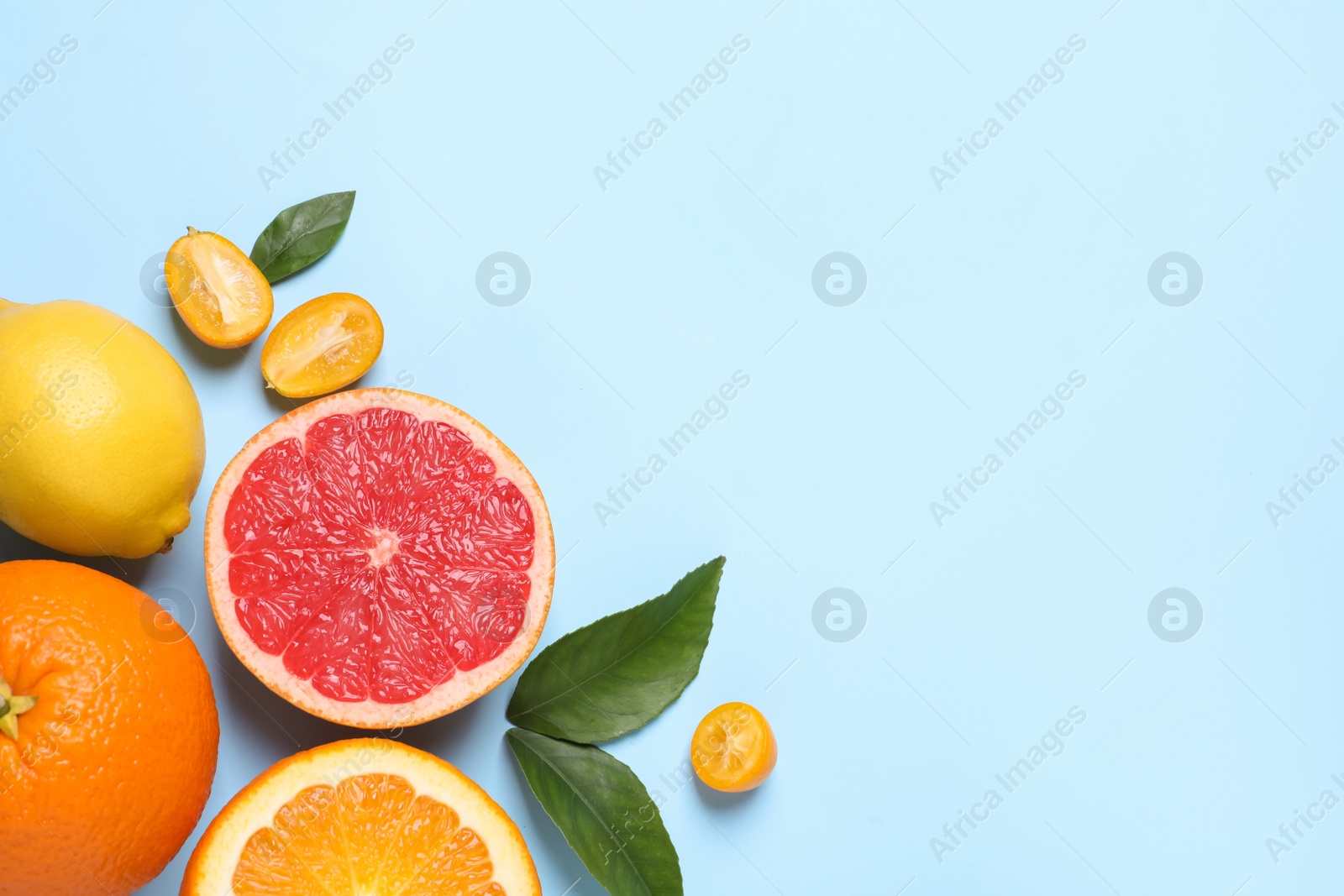 Photo of Fresh juicy citrus fruits with green leaves on light blue background, flat lay. Space for text