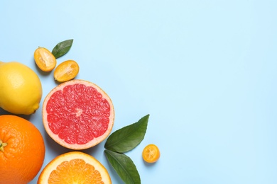 Photo of Fresh juicy citrus fruits with green leaves on light blue background, flat lay. Space for text