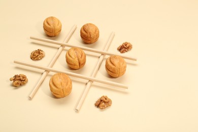 Tic tac toe game made with walnuts and cookies on beige background. Space for text