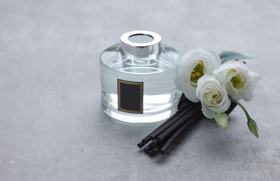 Photo of Reed sticks, glass bottle with aromatic liquid and eustoma flowers on gray marble table