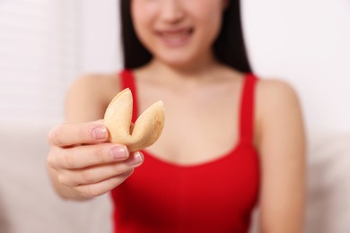 Photo of Young woman holding tasty fortune cookie with prediction indoors, closeup