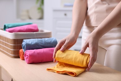 Photo of Woman rolling shirt at table in room, closeup. Organizing clothes